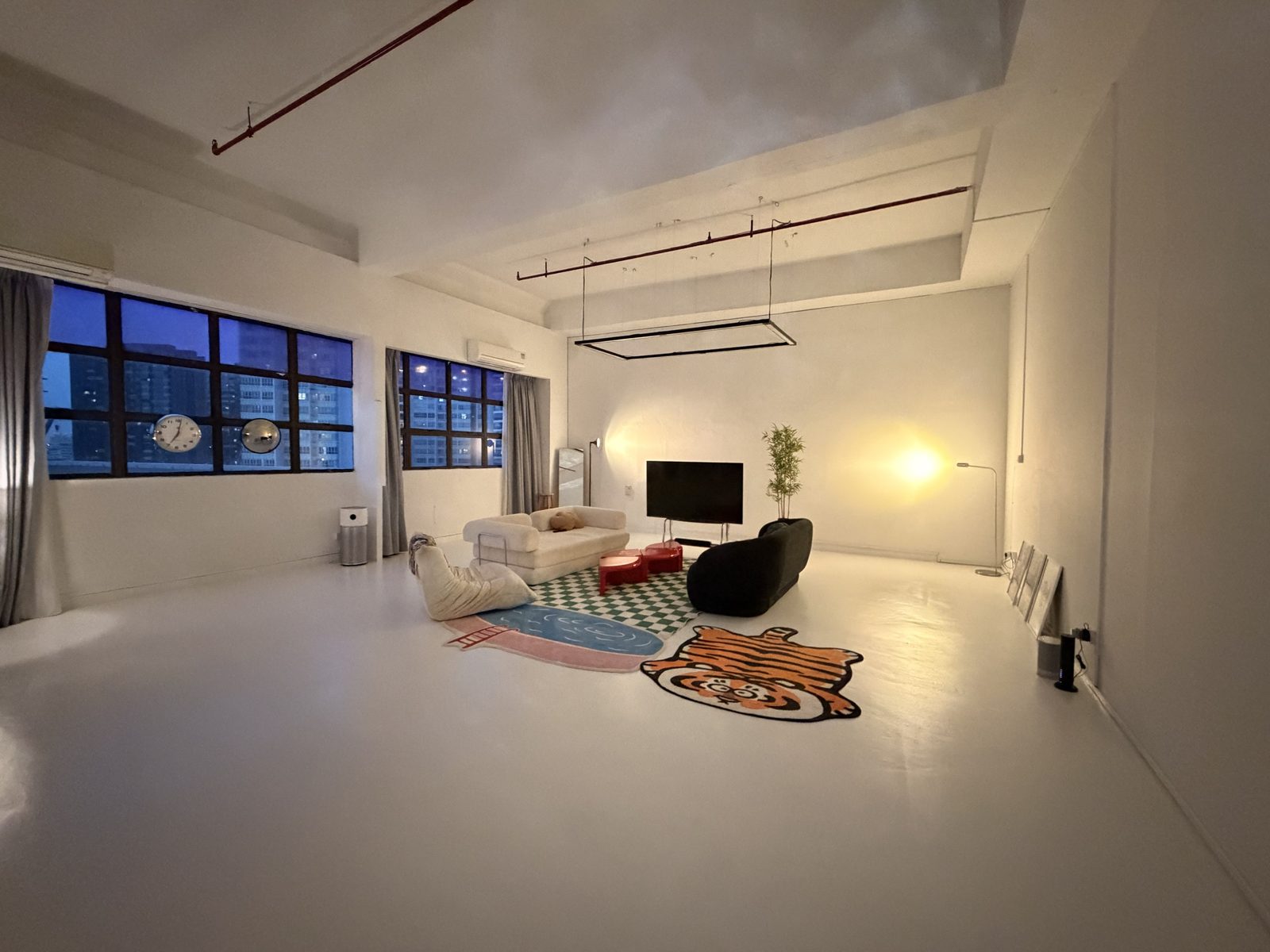 The studio at dusk: living set with sofas, red tables and a tiger rug under tall windows